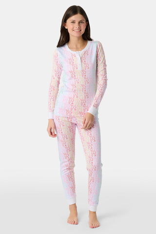 A girl with long brown hair stands barefoot, smiling and facing forward in Roller Rabbit Kids Monkey Juniper Pajamas—a matching set with a playful monkey print—against a plain white background.