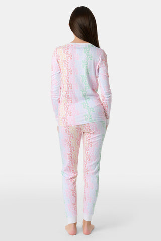 A girl with long brown hair stands barefoot, smiling and facing forward in Roller Rabbit Kids Monkey Juniper Pajamas—a matching set with a playful monkey print—against a plain white background.