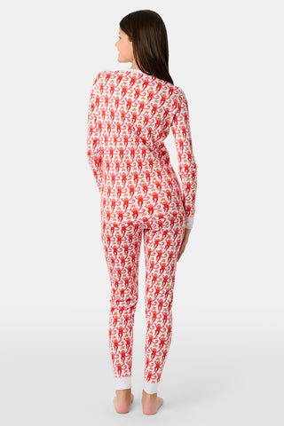 A child stands barefoot, facing away, wearing Kids Monkey Pajamas—a matching top and bottom set made of 100% Pima cotton with a red and white Christmas-themed pattern—against a plain light background.