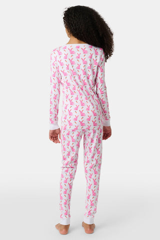 A young girl smiles barefoot in Roller Rabbit’s Kids Romy the Rabbit Pajamas, a soft Pima cotton long-sleeve set with a playful rabbit print; her brown hair frames her face against a simple, light background.