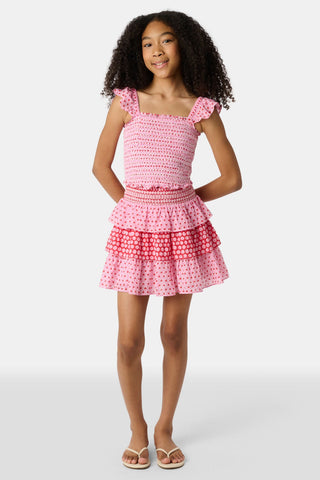 A child wears the Roller Rabbit Kids Starry Dot Sami Skirt in pink and red with star and polka dot patterns, paired with a pink smocked top, standing against a plain light background.