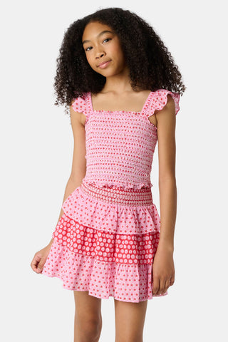 A young girl wears the Roller Rabbit Kids Starry Dot Tory Top in pastel pink with flutter sleeves, paired with a matching skirt featuring red stars and white polka dots. Only her torso and part of her face are visible.