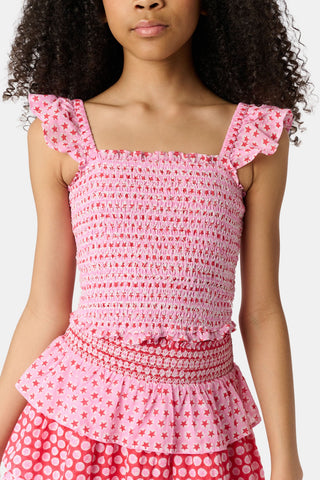 A young girl wears the Roller Rabbit Kids Starry Dot Tory Top in pastel pink with flutter sleeves, paired with a matching skirt featuring red stars and white polka dots. Only her torso and part of her face are visible.