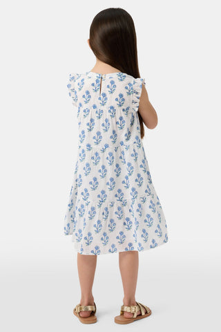 A young girl with long brown hair wears the Roller Rabbit Kids Rosa Ditsy Floral Pami Dress, made from cotton voile with blue-green block print and ruffled sleeves, standing against a plain light background, looking slightly to the side.