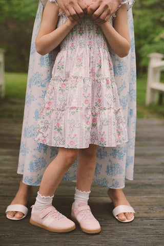 A child wears the Roller Rabbit Kids Monkey Block Stripe Tiny Ellie Nap Dress, standing on a wooden deck with an adult in a blue and white Roller Rabbit dress. Both face forward outdoors with greenery in the background.