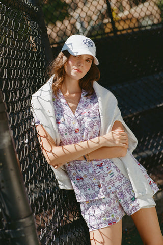 The Sigma Kappa Monkey Polo Pajamas by Roller Rabbit are a short-sleeve pajama set featuring matching shorts with a white background and colorful cartoon character pattern. Designed for comfort, they include a front button placket and an elastic waistband.