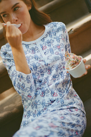 A woman in Roller Rabbit Delta Gamma Monkey Pajamas sits on steps, eating from a cup of ice cream topped with rainbow sprinkles using a white plastic spoon.