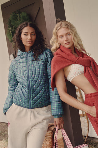 A woman wearing a SOPHISTICA Plaid Hearts Reversible Puffer Jacket, a hooded, zip-front nylon puffer in an emerald green and blue plaid pattern accented by small pink hearts.