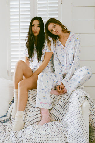 Roller Rabbit Print. Two women sitting on a bed wearing matching pajamas in a cozy room.