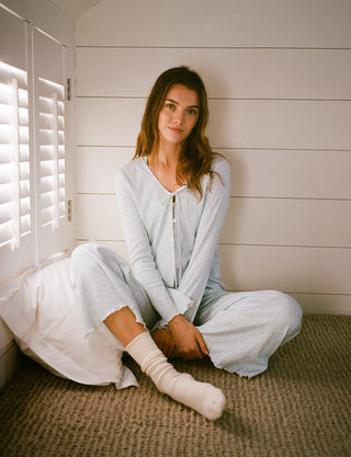Roller Rabbit PJs. Woman sitting on a carpeted floor wearing a light gray outfit in a room with white walls and a window.
