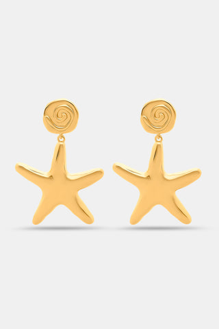 A close-up shows Roller Rabbit Starfish Drop Earrings—gold-tone brass danglers with a starfish charm on a textured stud—worn by someone with curly dark hair and medium-toned skin, highlighting this summery accessory.