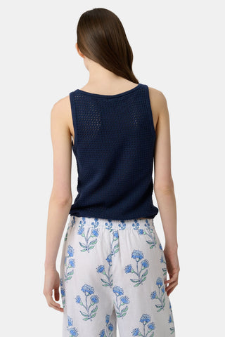 A woman wears the Roller Rabbit Pointelle Sasha Sweater Tank in navy with a textured open-weave design, paired with white shorts featuring blue floral prints. She is shown from shoulders to waist, looking slightly to the side.