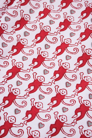 A person stands barefoot, lower half visible, wearing Roller Rabbit's Campus Mens Lovely Monkey Simon Pant—white Pima cotton pants with a red and black monkey pattern and a drawstring waist, one hand in their pocket.