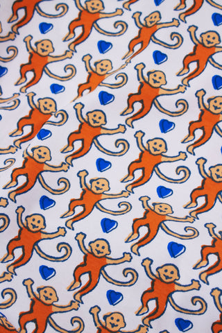 A woman with long brown hair models the Roller Rabbit Campus Lovely Monkey Polo Pajamas—an orange and navy animal print short-sleeved button-up top with matching shorts—against a plain light backdrop.