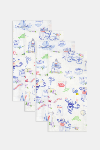 Set of four white Ecovero linen napkins by Roller Rabbit, featuring whimsical, cartoon-like beach-themed illustrations—monkeys, sailboats, houses, bicycles, and seashells—in vibrant blue, red, green, and purple hues. Made in India. Product name: Monkey On The Vineyard Napkin Set Of 4.