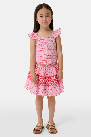 A child wears the Roller Rabbit Kids Starry Dot Sami Skirt in pink and red with star and polka dot patterns, paired with a pink smocked top, standing against a plain light background.