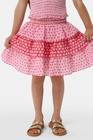 A child wears the Roller Rabbit Kids Starry Dot Sami Skirt in pink and red with star and polka dot patterns, paired with a pink smocked top, standing against a plain light background.