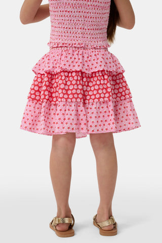A child wears the Roller Rabbit Kids Starry Dot Sami Skirt in pink and red with star and polka dot patterns, paired with a pink smocked top, standing against a plain light background.
