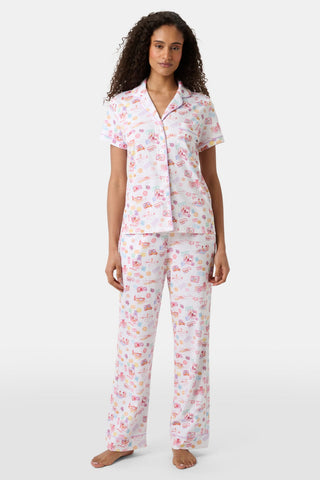 A woman with curly hair models the Roller Rabbit Summer Memories Fiora Pajamas, a Pima cotton set with a colorful sushi print, including a short-sleeve button-up top and long pants, against a white background.