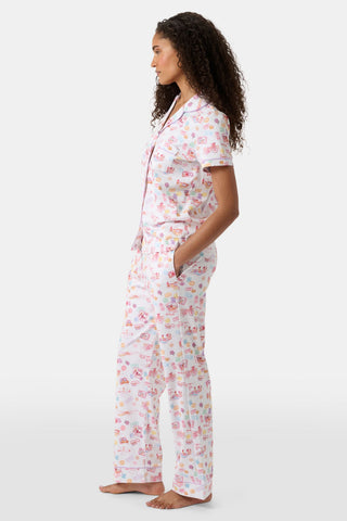 A woman with curly hair models the Roller Rabbit Summer Memories Fiora Pajamas, a Pima cotton set with a colorful sushi print, including a short-sleeve button-up top and long pants, against a white background.