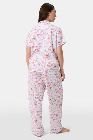 A woman with curly hair models the Roller Rabbit Summer Memories Fiora Pajamas, a Pima cotton set with a colorful sushi print, including a short-sleeve button-up top and long pants, against a white background.