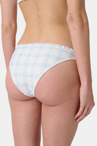 A person wearing the Roller Rabbit Sun Check Eyelet Sydney Bikini Bottom, featuring blue gingham with ruffled edges, is shown from mid-torso to upper thigh against a plain background.