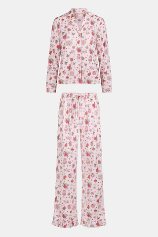 A person wearing pink long-sleeved Seasons Soiree Kate Pajamas with a ruffled hem and a repeating print of holiday sweets and treats.