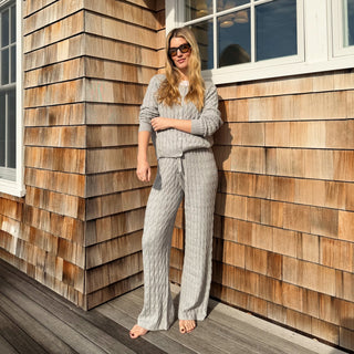 Woman in a gray outfit standing on a wooden deck next to a house with wooden siding.