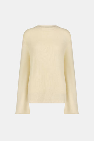 A woman wearing the Roller Rabbit Soleil Sweater, a cream cashmere blend pullover with wide sleeves, paired with patterned blue and white pants, stands against a plain white background.