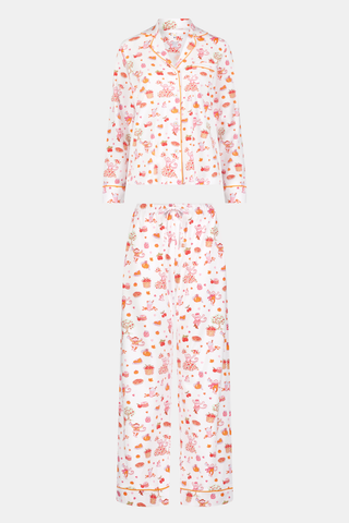 A woman stands barefoot against a plain white background, hands in pockets, wearing the Roller Rabbit Sweater Weather Long Sleeve Polo Pajamas—a floral pink and white set featuring a long-sleeved polo top and matching pants.