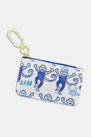 The Roller Rabbit Tri Delta Monkey Coin Pouch is a small zippered pouch featuring a blue monkey pattern, the number 1888, and a small blue flame printed on a white cotton canvas background with a protective poly coating for water resistance. It includes a gold carabiner clip and a blue zipper.