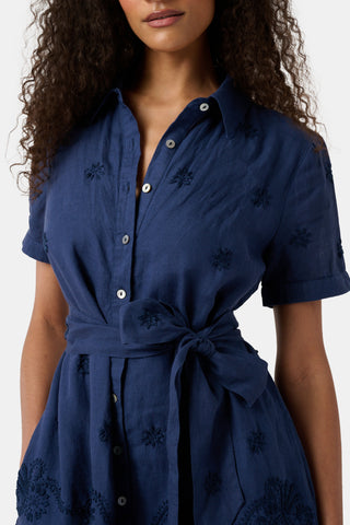 A woman models the Roller Rabbit Vanna Embroidery Margaret Dress—a short-sleeve navy linen shirtdress with a belted waist—standing against a plain light background.