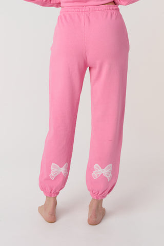 A person wears the Roller Rabbit Vintage Valentine Sweatpants—pink fleece with a drawstring waist and white heart designs—standing barefoot against a plain light background, showcasing only the lower half of their body.