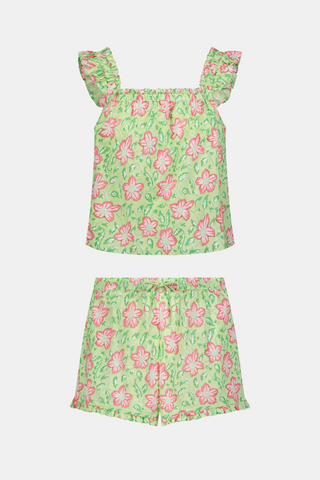 Three women are in a library. One wears the Verdant Floral Pipette Dress by Roller Rabbit—a green floral minidress—and stands with her hand on her chin. Another sits on a patterned sofa with her eyes closed, and bookshelves are visible in the background.