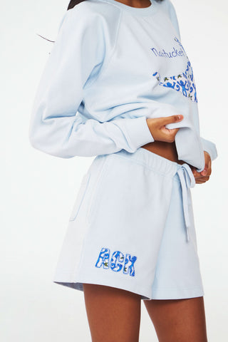 A person wears the Roller Rabbit ACK Applique Shortie, paired with a light blue whale-decorated Nantucket sweatshirt. The shortie features patchwork "ACK" letters near the hem.
