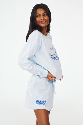 A person wears the Roller Rabbit ACK Applique Shortie, paired with a light blue whale-decorated Nantucket sweatshirt. The shortie features patchwork "ACK" letters near the hem.