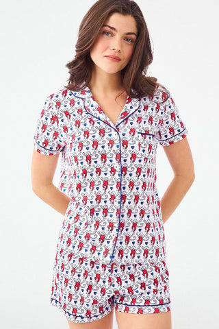 A woman stands with hands behind her back in Roller Rabbit's Campus Lovely Monkey Polo Pajamas, a short-sleeved, button-up red and navy romper with playful patterns—perfect sleepwear for showing your school spirit.