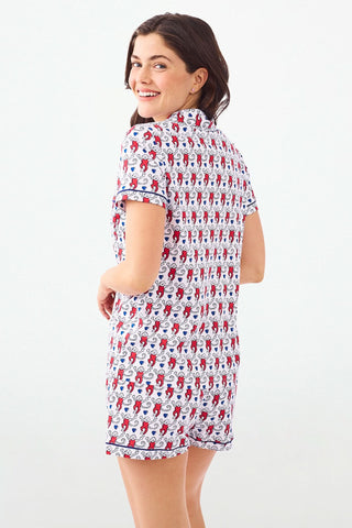 A woman stands with hands behind her back in Roller Rabbit's Campus Lovely Monkey Polo Pajamas, a short-sleeved, button-up red and navy romper with playful patterns—perfect sleepwear for showing your school spirit.