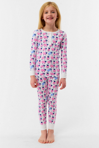 A smiling young girl stands barefoot in Kids Sammy The Sheep Pajamas by Roller Rabbit, posing against a white backdrop to showcase stylish children's sleepwear.