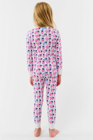 A smiling young girl stands barefoot in Kids Sammy The Sheep Pajamas by Roller Rabbit, posing against a white backdrop to showcase stylish children's sleepwear.
