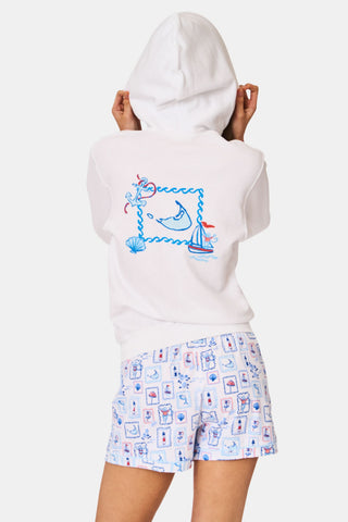 A person wearing the Roller Rabbit ACK Zip Up hoodie, featuring a blue and red nautical design on the back, paired with patterned shorts and standing with their back to the camera and hood up.