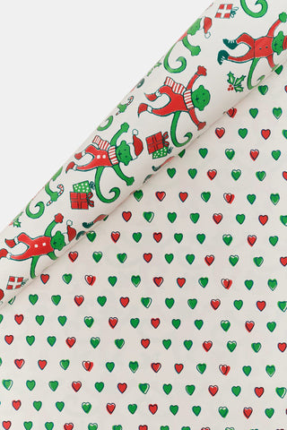 Monkey Mas/Holiday Hearts Wrapping Paper featuring a pattern of green monkeys in Santa hats and outfits on one side, and a pattern of small Holiday Hearts on the other.
