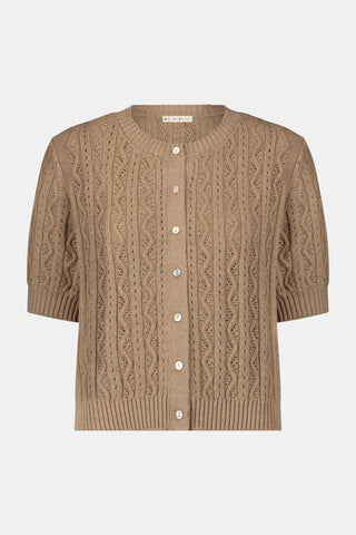 A woman wears the Roller Rabbit Zig Zag Pointelle Nyla Cardigan, a short-sleeved, walnut brown button-front sweater with circular patterns, paired with a light blue patterned skirt.